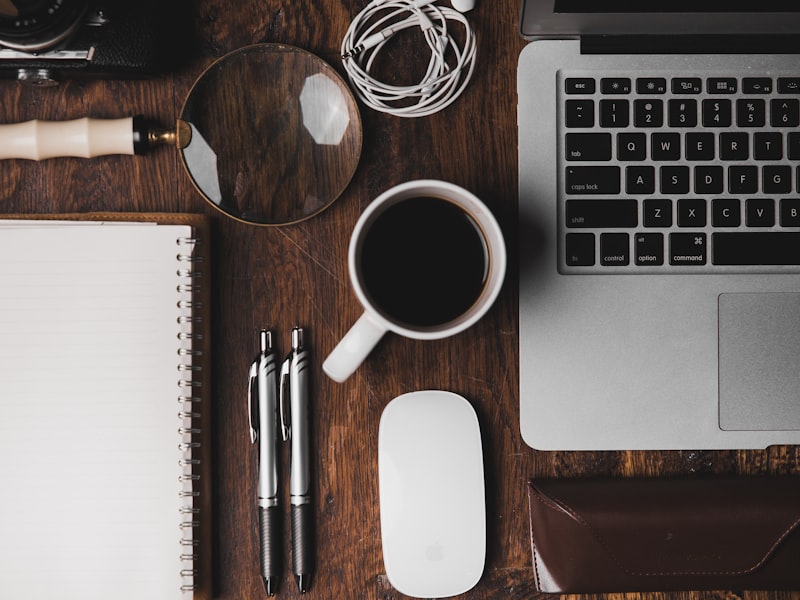 Vue de dessus d'un poste de travail avec MacBook, café, loupe et stylos — outils de l'audit SEO