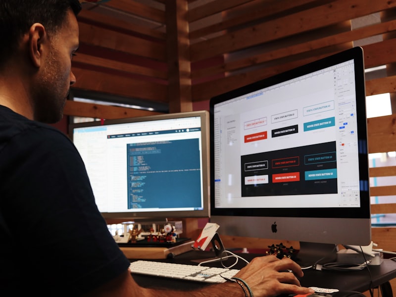 Designer travaillant sur deux écrans — bibliothèque de boutons UI et code à droite